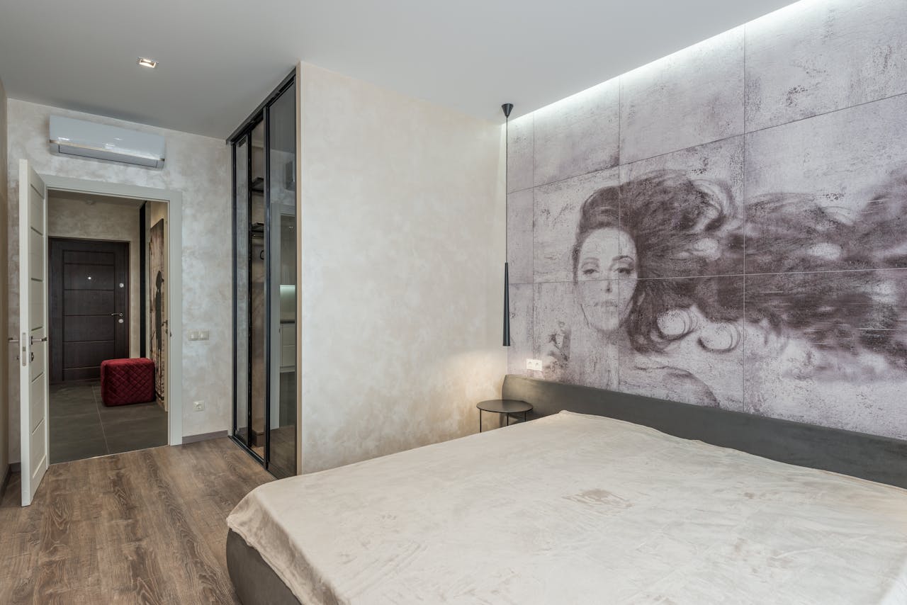 Comfortable bed placed near wall with creative wallpaper in modern bedroom with mirrored closet and parquet floor